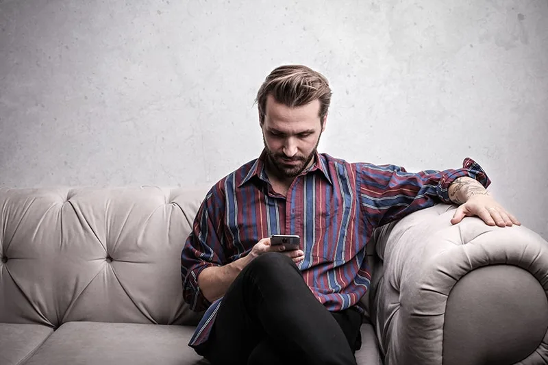 Ein Mann sitzt auf der Couch und liest eine Nachricht von einem Smartphone