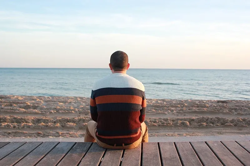 Ein Mann sitzt allein auf einer Holztafel und blickt auf den Ozean