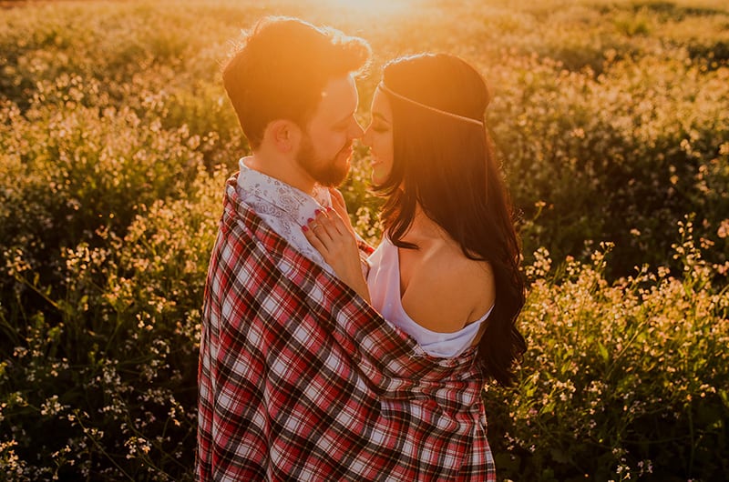 Ein Mann und eine Frau, die sich gerade mit einer Decke küssen wollen, während sie in der Natur stehen