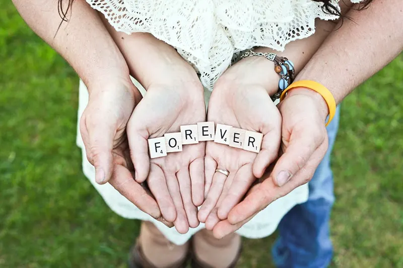 ein Paar, das "Forever" -Scrabble-Buchstaben auf den Handflächen hält