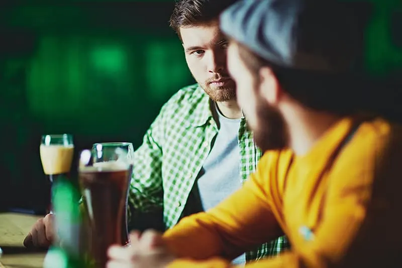 Ein introvertierter Mann, der seinen Freund ansieht, während er an der Bar sitzt