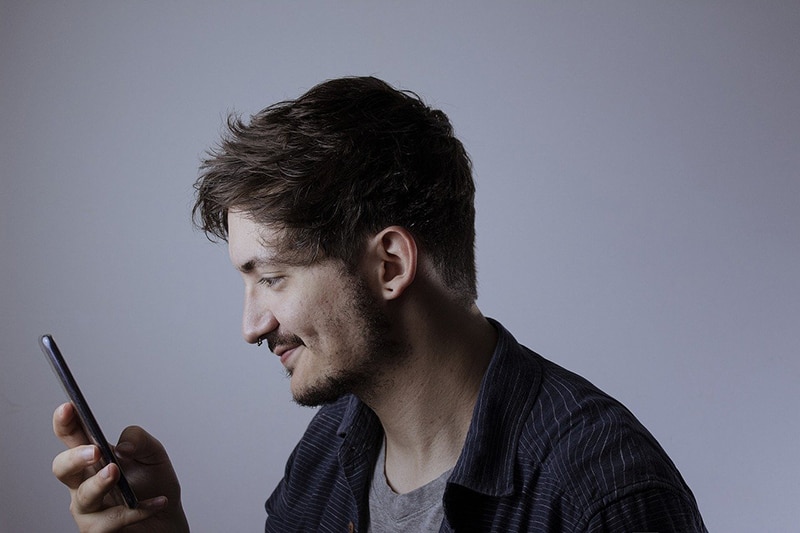 ein lächelnder Mann, der ein Smartphone hält und es benutzt