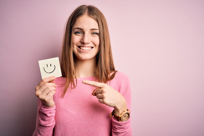 eine Frau, die Erinnerungspapier mit Lächeln-Emoji-Nachricht hält und mit dem Finger auf das Papier zeigt