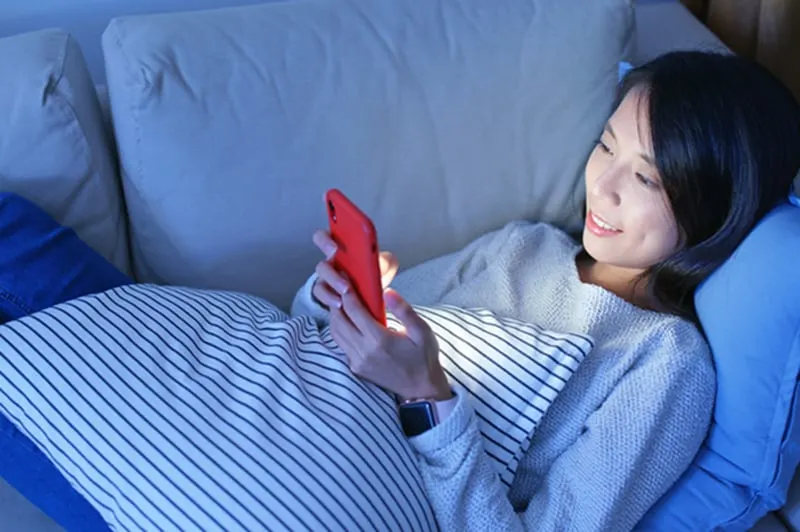 eine Frau, die abends auf der Couch liegt und ein Smartphone benutzt