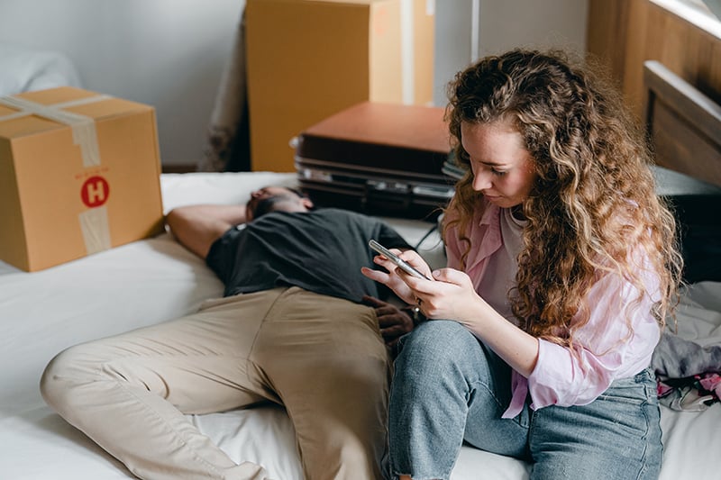 Eine Frau überprüft das Telefon ihres Freundes, während er auf dem Bett ein Nickerchen macht