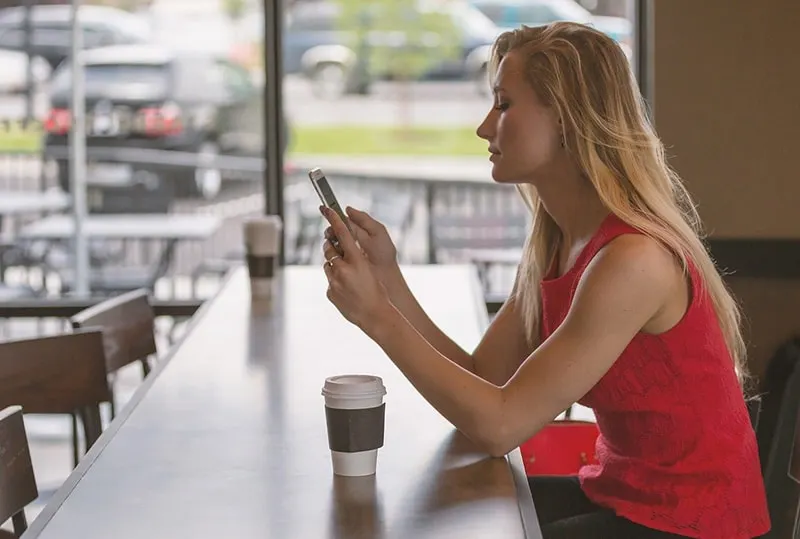 eine Frau, die eine Nachricht auf ihrem Smartphone liest, während sie in einem Café sitzt