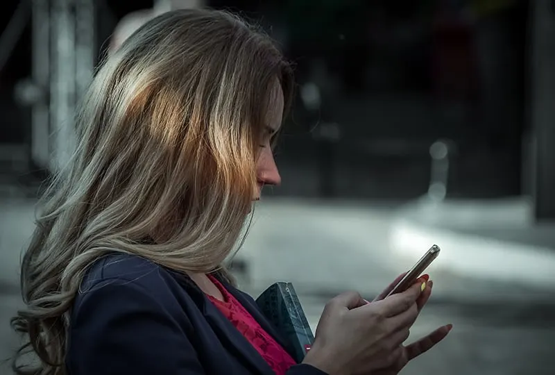 eine Frau, die eine Nachricht auf ihrem Smartphone tippt, während sie draußen steht