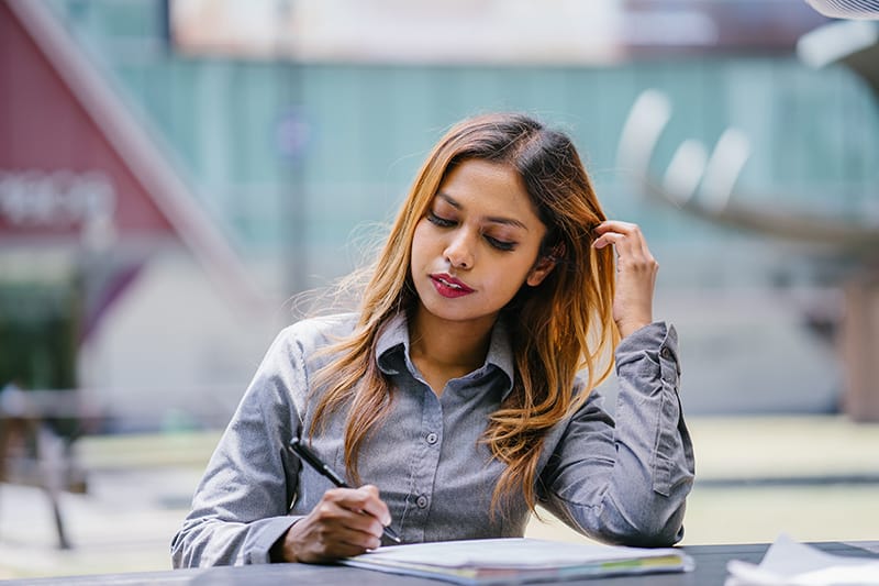 eine Frau, die einen Stift hält und ihre Haare berührt, während sie am Tisch sitzt