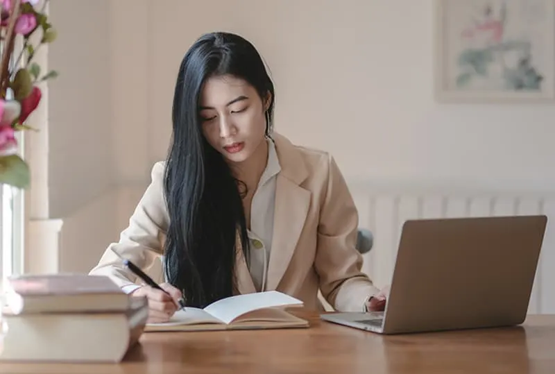 eine Frau, die in ein Notizbuch schreibt, während sie im Büro arbeitet