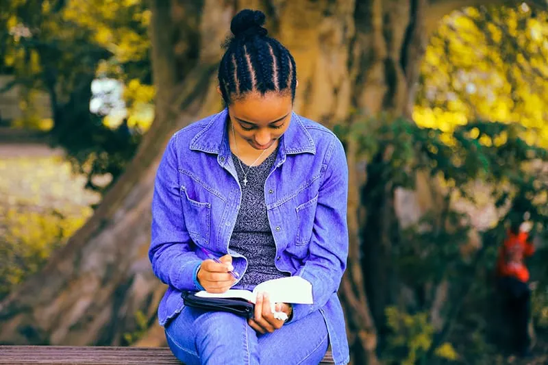 eine Frau, die in ein Notizbuch schreibt, während sie auf der Bank sitzt