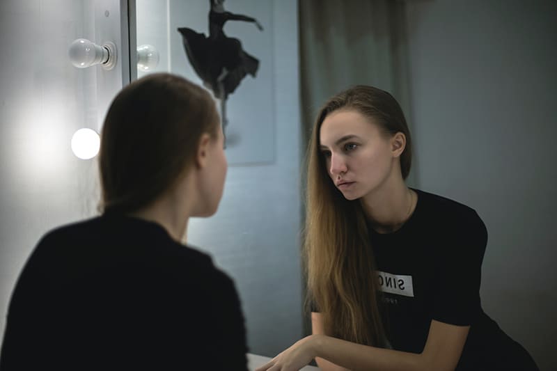 eine Frau, die sich mit traurigem Gesichtsausdruck in den Spiegel schaut