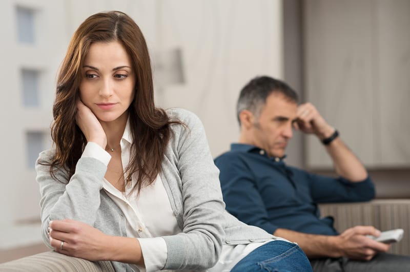 eine Frau, die sich schuldig fühlt, während sie auf der Couch neben einem Mann sitzt, der fernsieht