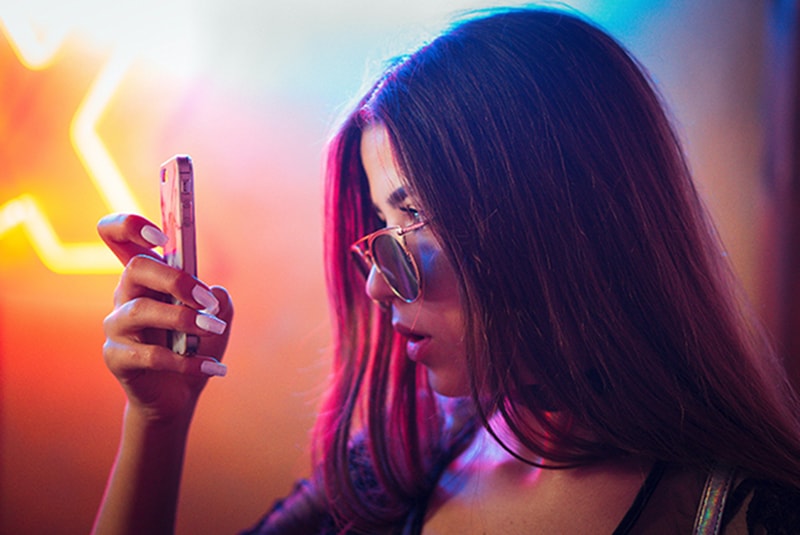 eine Frau, die Smartphone mit Unglauben betrachtet, während sie in der Nähe von Neonlichtern steht