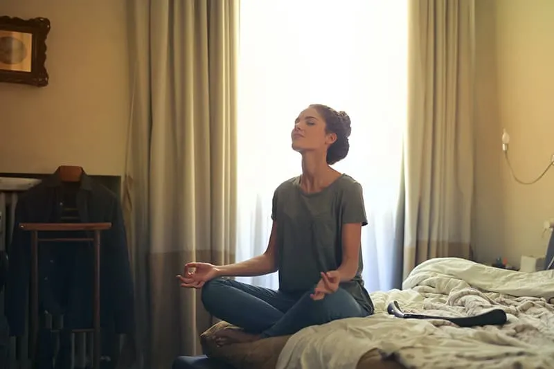 eine Frau, die in einem Haus meditiert, während sie im Schlafzimmer sitzt