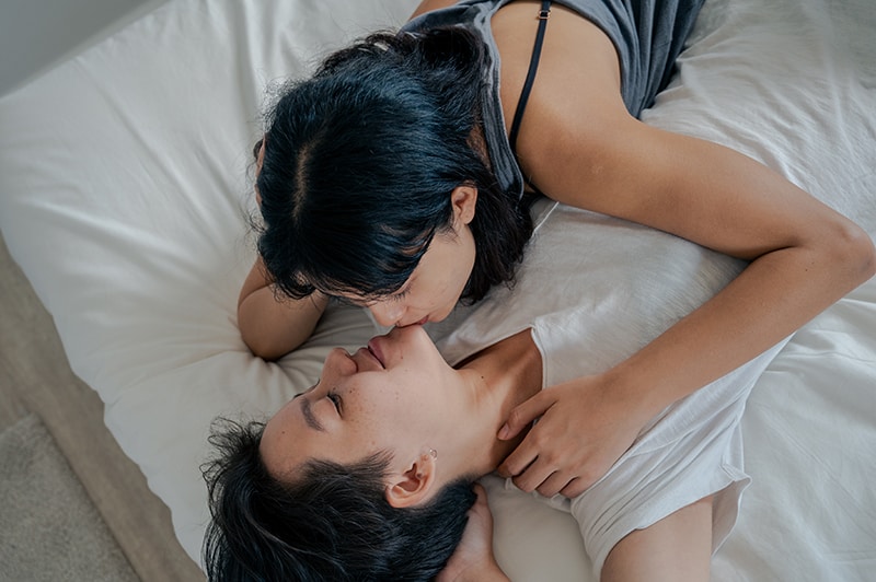 Eine Frau küsst einen Mann am Kinn, während beide auf dem Bett liegen