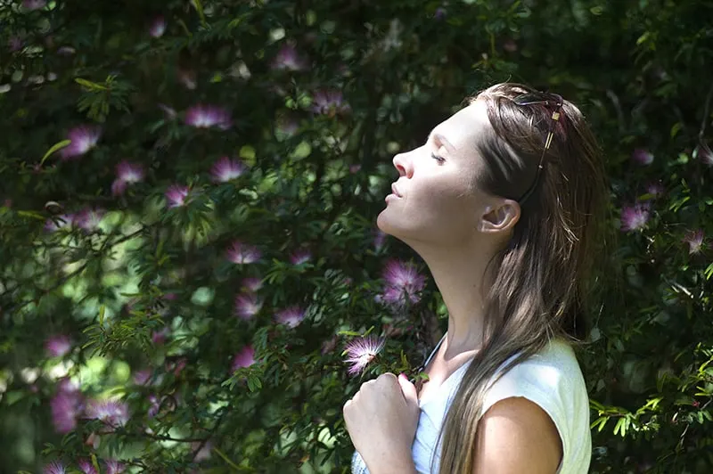 eine Frau mit geschlossenen Augen, die dem Sonnenlicht zugewandt ist, während sie in der Nähe der Pflanzen steht