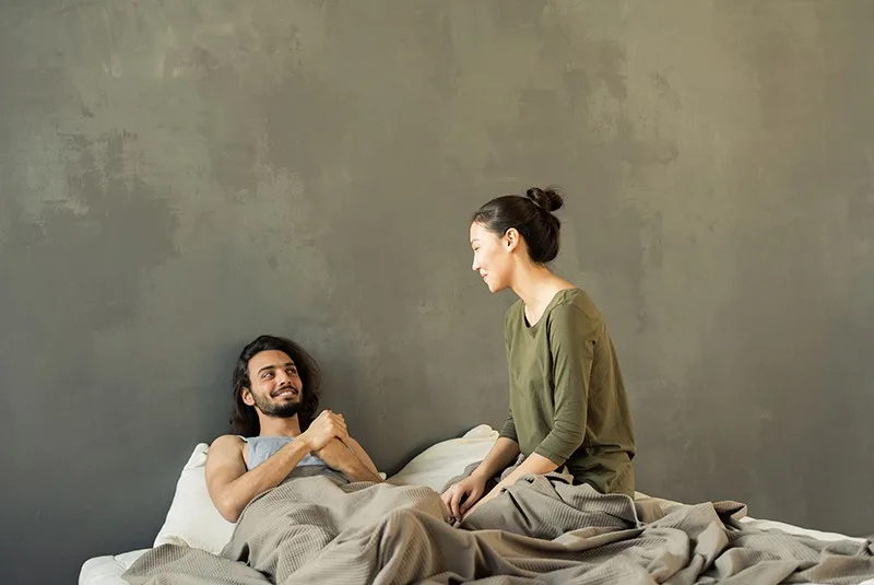 Eine Frau sitzt auf dem Bett neben einem Mann, der im Bett liegt und zusammen lacht