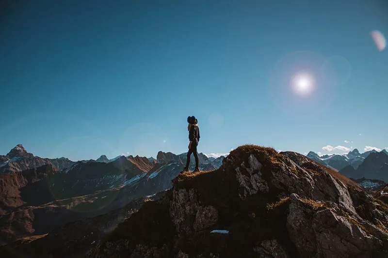 eine Person, die auf der Klippe mit Blick auf die Berge steht