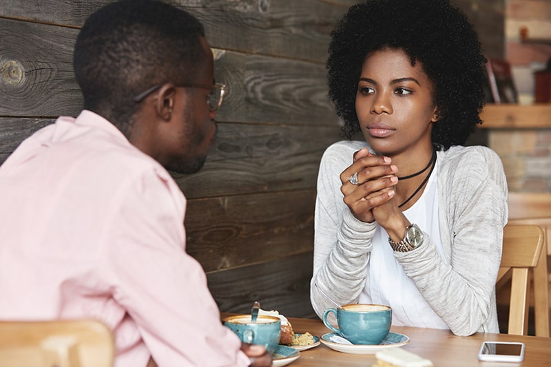 eine ernste Frau, die einen Mann während eines Gesprächs ansieht, während sie im Café sitzt