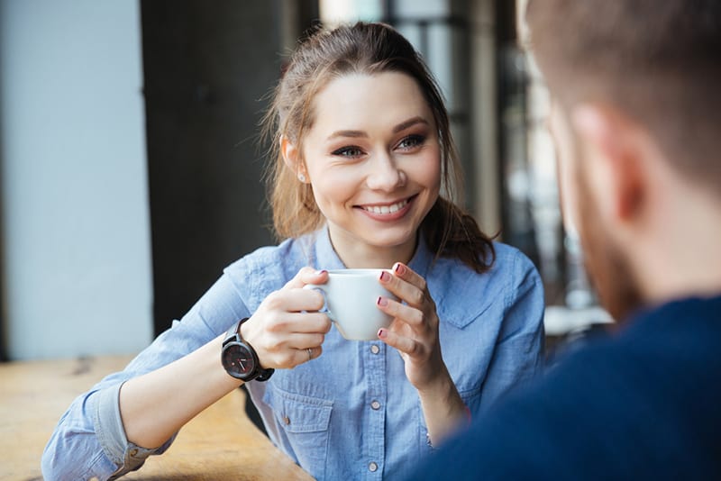 eine fröhliche Frau, die mit einem männlichen Freund im Café sitzt und Kaffee trinkt