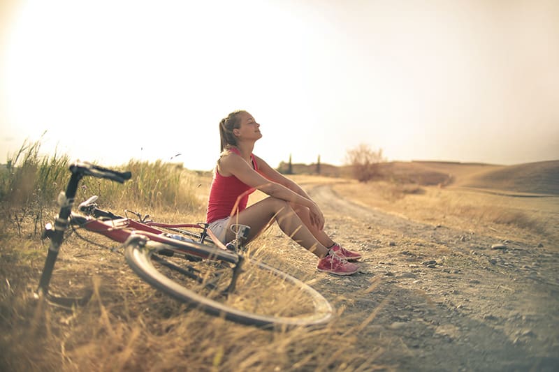 eine glückliche Frau, die auf dem Boden sitzt, während sie sich vom Fahrradfahren ausruht