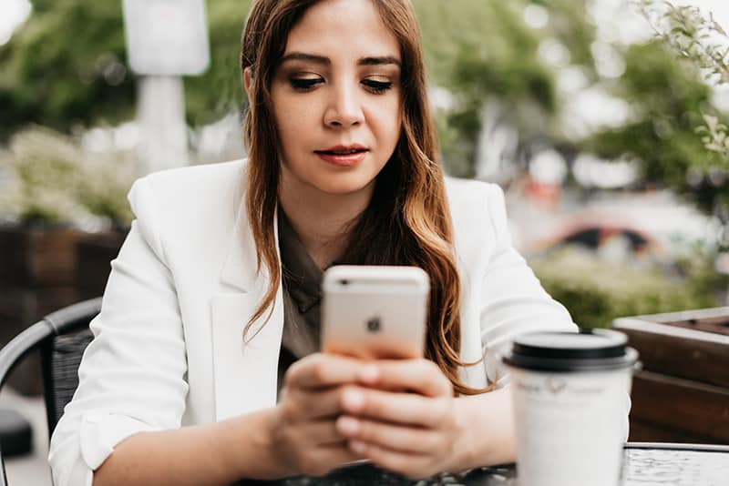eine interessierte Frau, die eine Nachricht auf dem Smartphone liest, während sie im Café sitzt