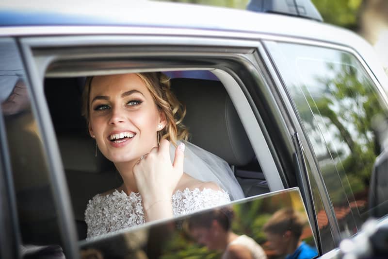 eine lächelnde Braut, die im Auto sitzt und durch das Fenster schaut