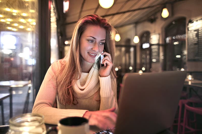eine lächelnde Frau, die auf dem Smartphone spricht, während sie in der Cafeteria sitzt