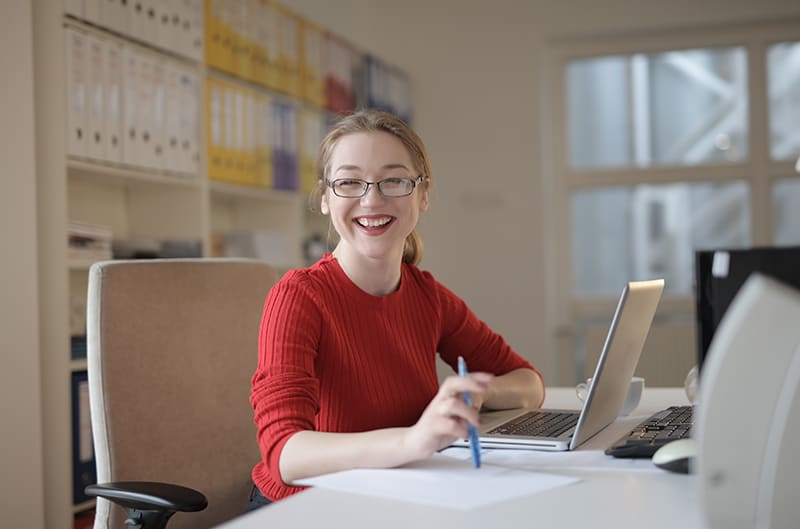 eine lächelnde Frau, die im Büro vor dem Laptop sitzt