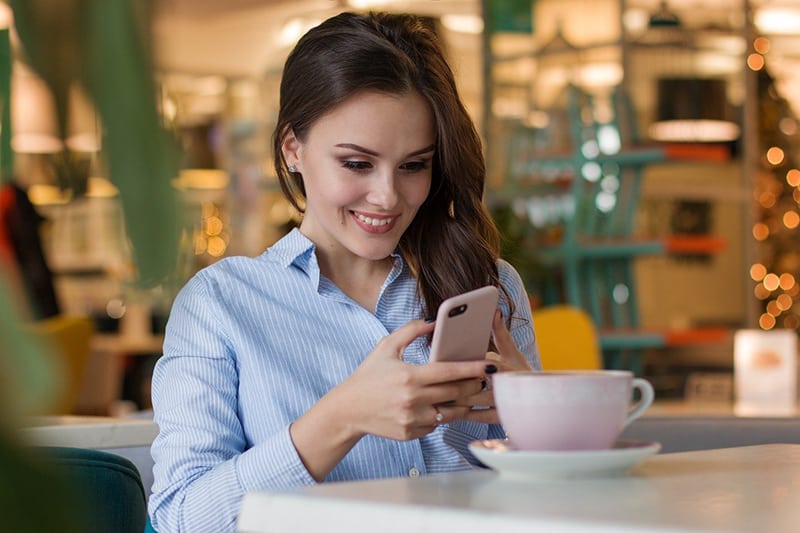 eine lächelnde Frau, die ein Smartphone benutzt, während sie im Kaffee sitzt