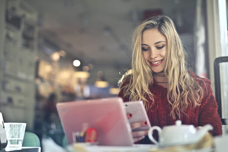 eine lächelnde Frau, die eine Nachricht von einem Smartphone liest, während sie im Cafe sitzt