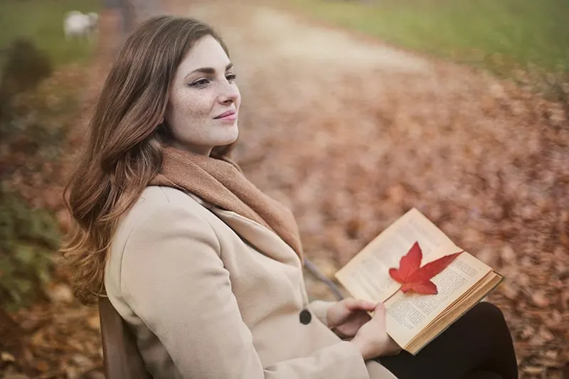 eine nachdenkliche Frau, die auf der Bank im Park sitzt und ein Buch hält