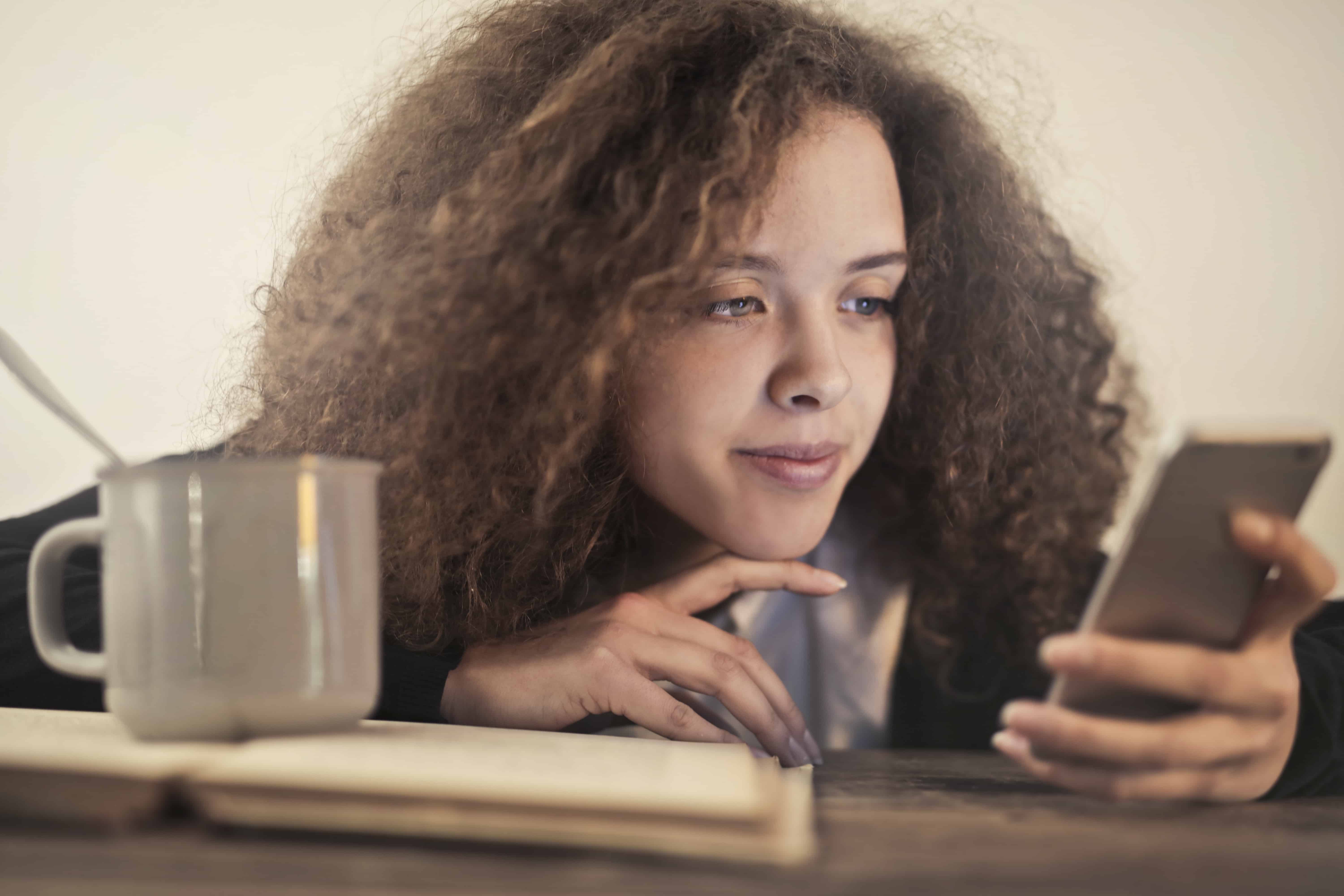 eine nachdenkliche Frau, die sich auf den Tisch stützt, während sie ein Smartphone benutzt