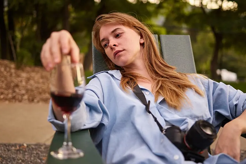 eine nachdenkliche Frau, die auf der Sonnenliege sitzt und ein Glas Wein berührt