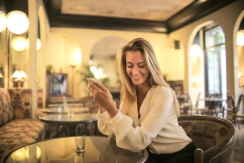eine positive Frau, die alleine in der Bar sitzt und ein Smartphone hält