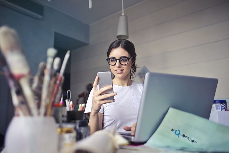 eine überraschte Frau, die auf das Smartphone schaut, während sie am Schreibtisch sitzt