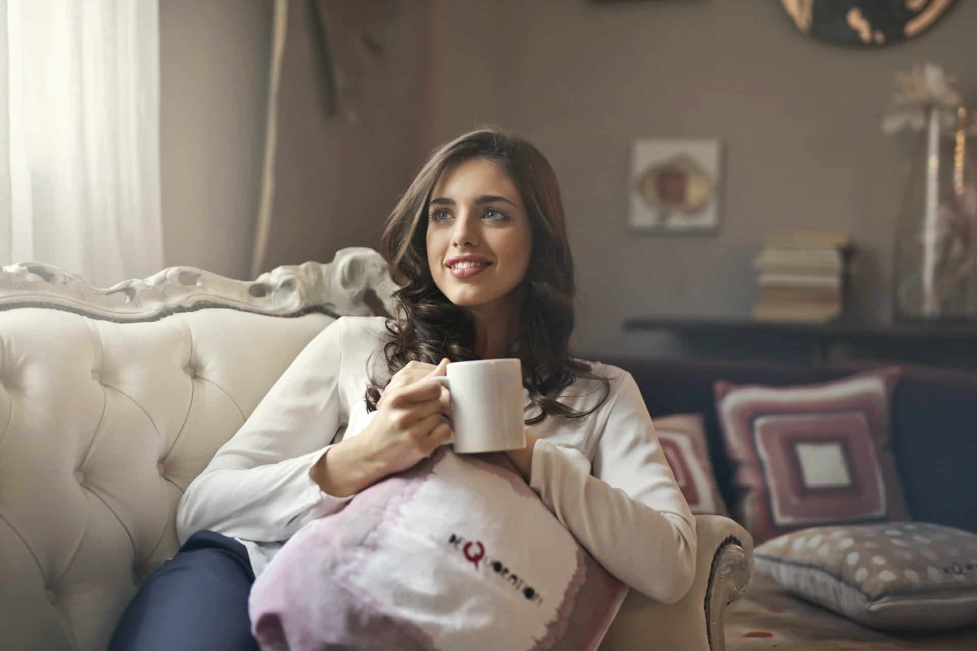 lächelnde Frau, die auf der Couch sitzt und während einer Pause Kaffee trinkt