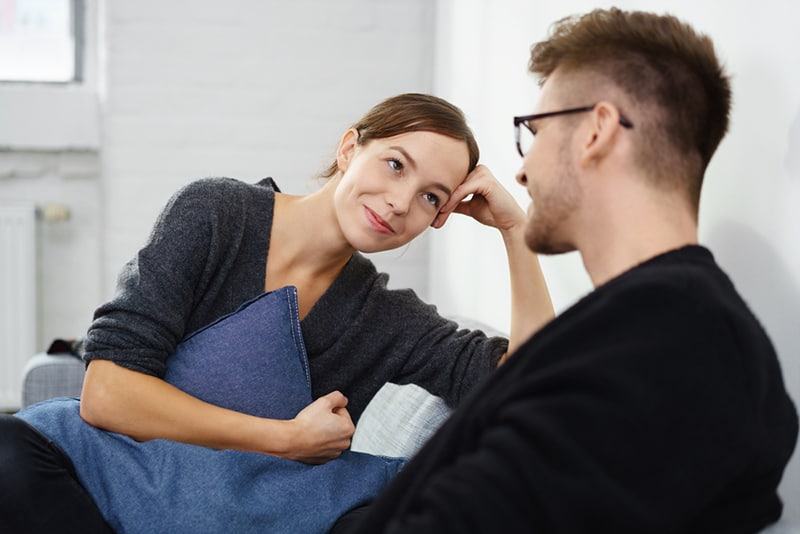 lächelnde Frau, die einen Mann beim Sitzen auf der Couch betrachtet