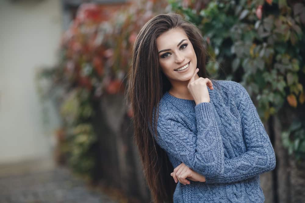 schöne Brünette, die draußen in einem grauen Pullover steht