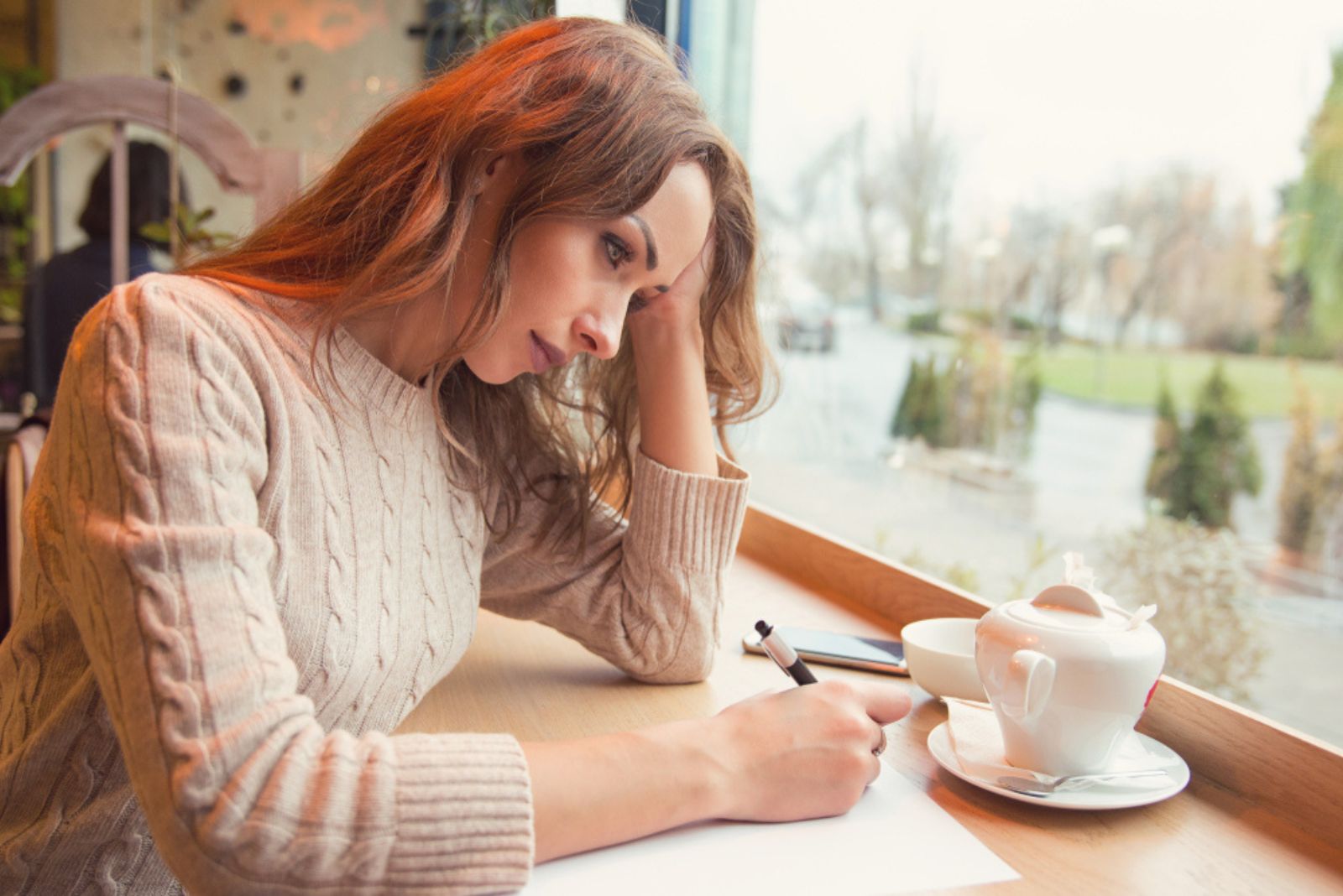 traurige Frau schreibt einen Brief im Cafe