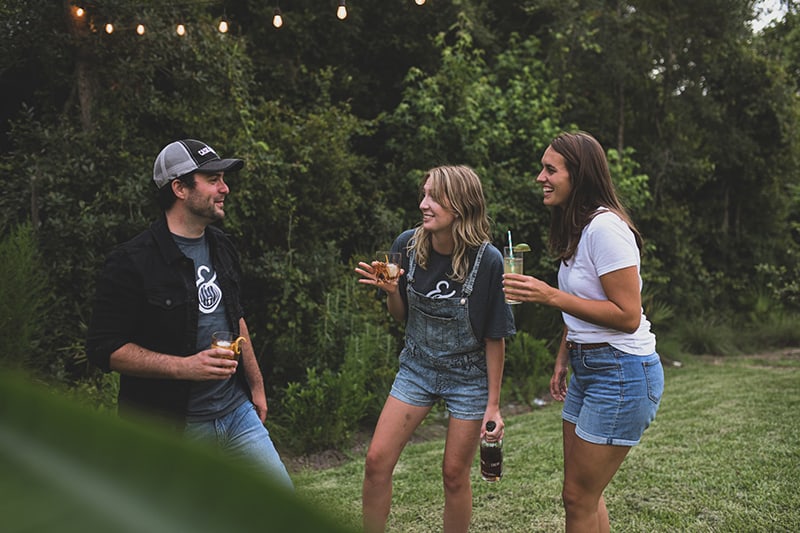 zwei Mädchen sprechen mit einem introvertierten Mann, während sie zusammen auf einer Party etwas trinken