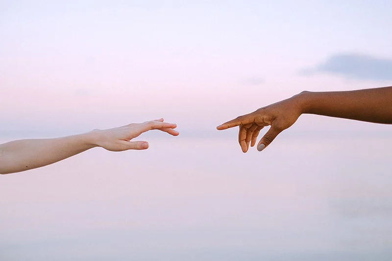 Zwei Personen erreichen sich bei Sonnenuntergang gegenseitig die Hand