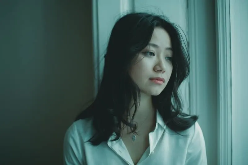 Am Fenster steht eine traurige Chinesin in einem weißen Hemd