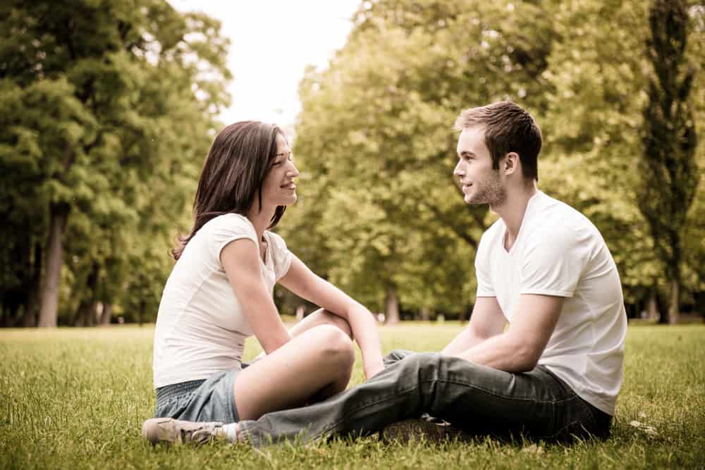 Auf dem Rasen im Park sitzt eine glückliche Frau mit einem Mann und redet