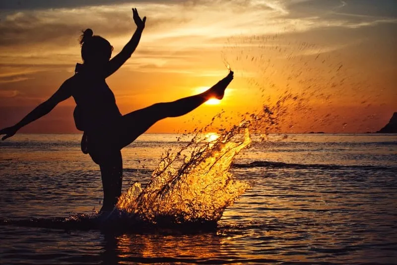 Bei Sonnenuntergang steht eine Frau im Flachwasser des Meeres
