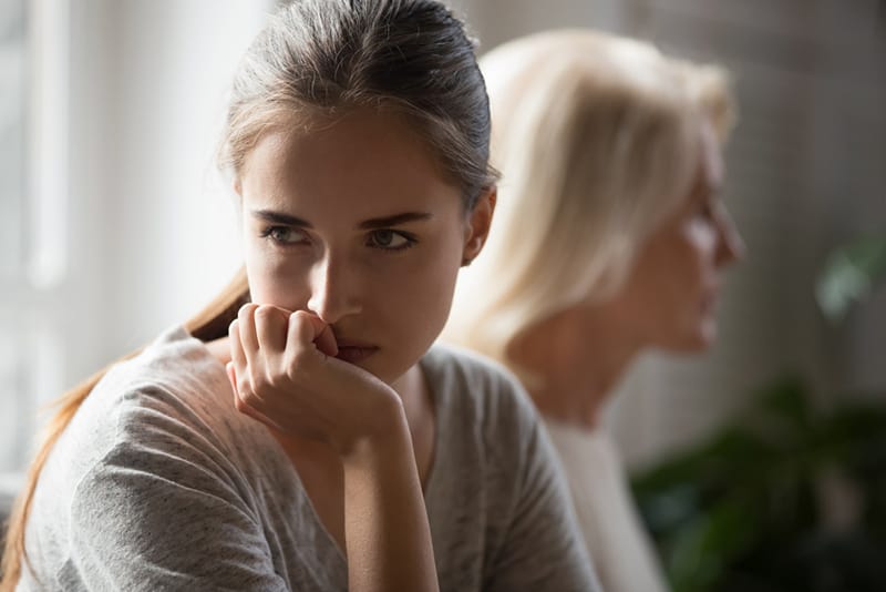 Beleidigte erwachsene Tochter und ältere Mutter sitzen Rücken an Rücken und vermeiden es, nach dem Kampf zu reden