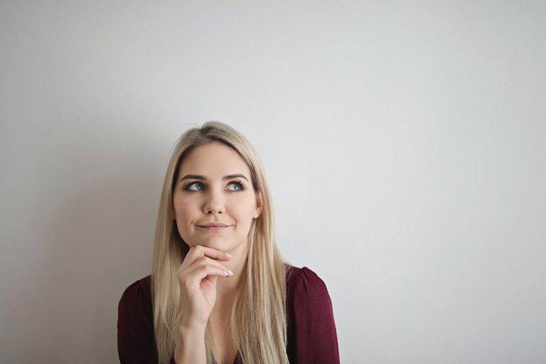 eine Frau mit blonden Haaren denkt und berührt das Kinn mit einer Hand
