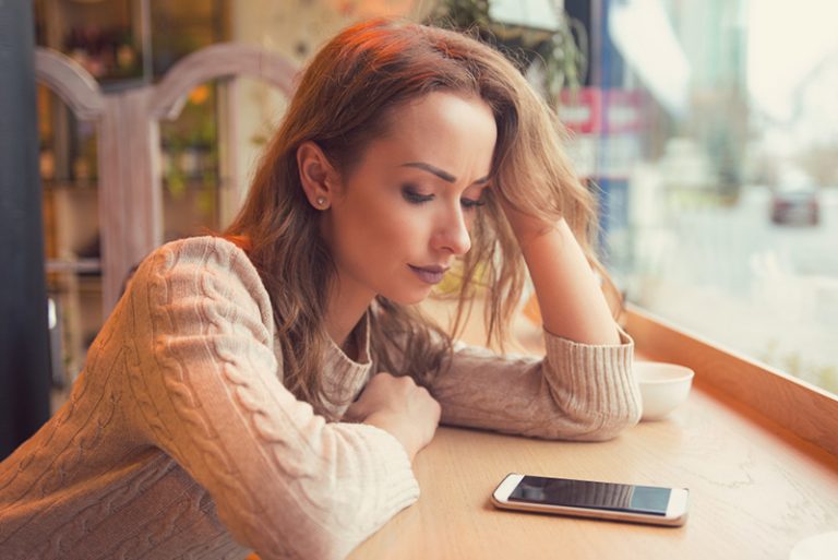 ein unglückliches Mädchen, das Smartphone betrachtet, während es im Café sitzt