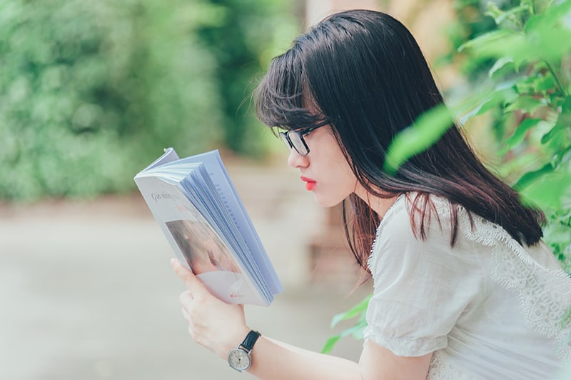 eine Frau, die ein Buch liest, während sie in der Nähe der Pflanzen sitzt