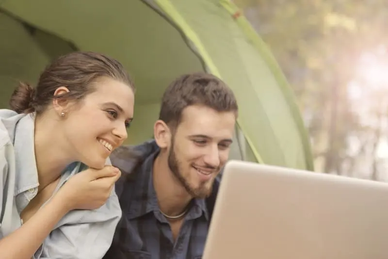 Draußen benutzen ein Mann und eine Frau mit einem Lächeln einen Laptop
